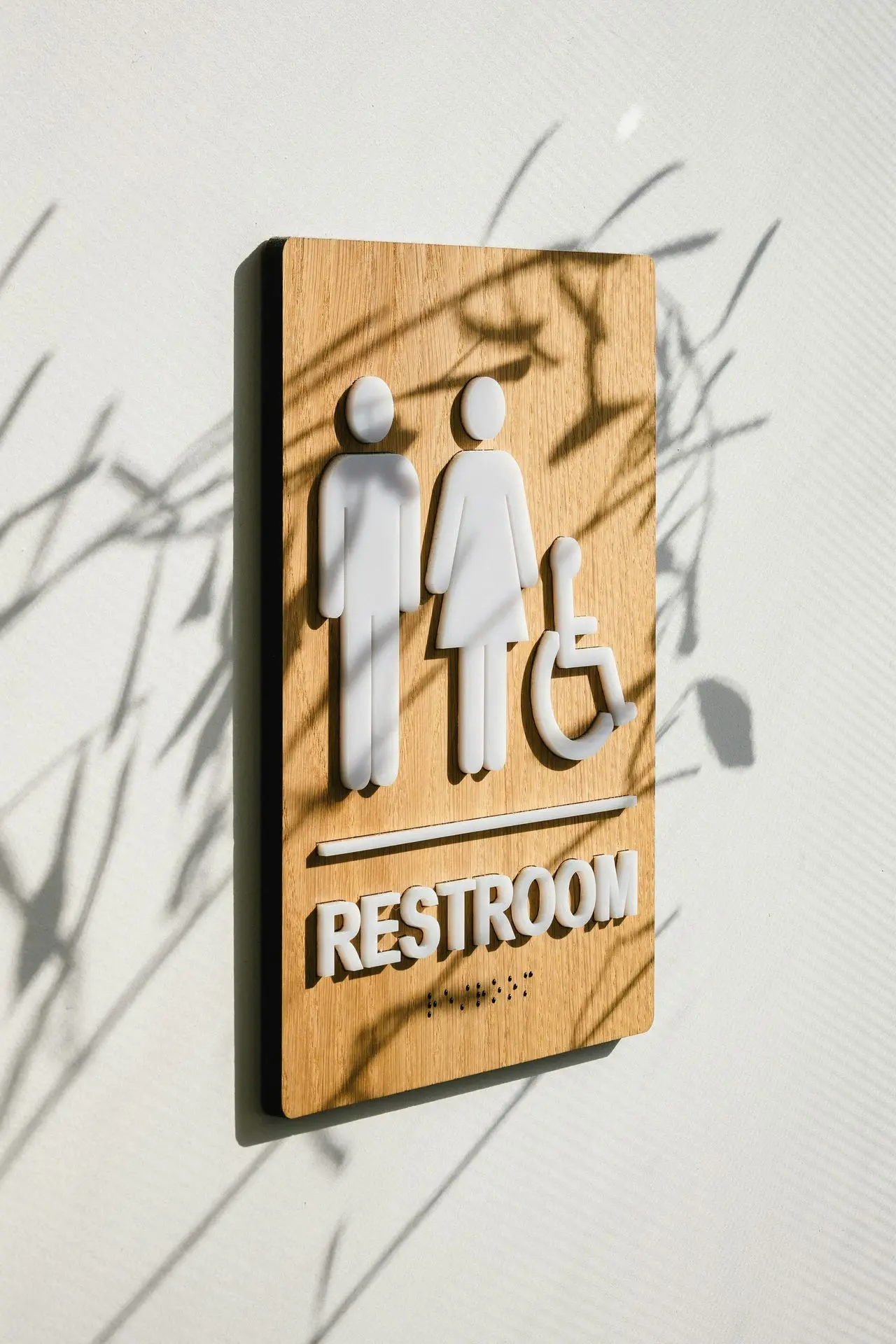 Wooden restroom sign featuring icons for male, female, and wheelchair accessibility, with braille underneath.