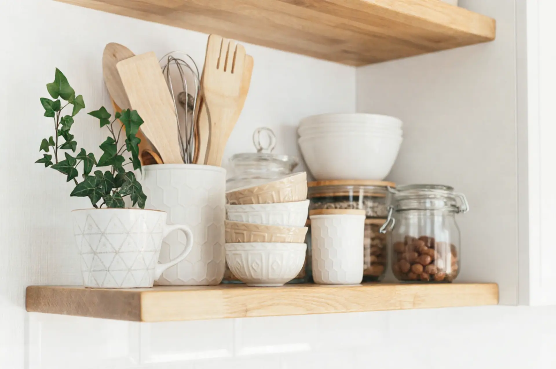 Open wooden kitchen shelf with white ceramic bowls, wooden utensils in a crock, and a small potted ivy plant.