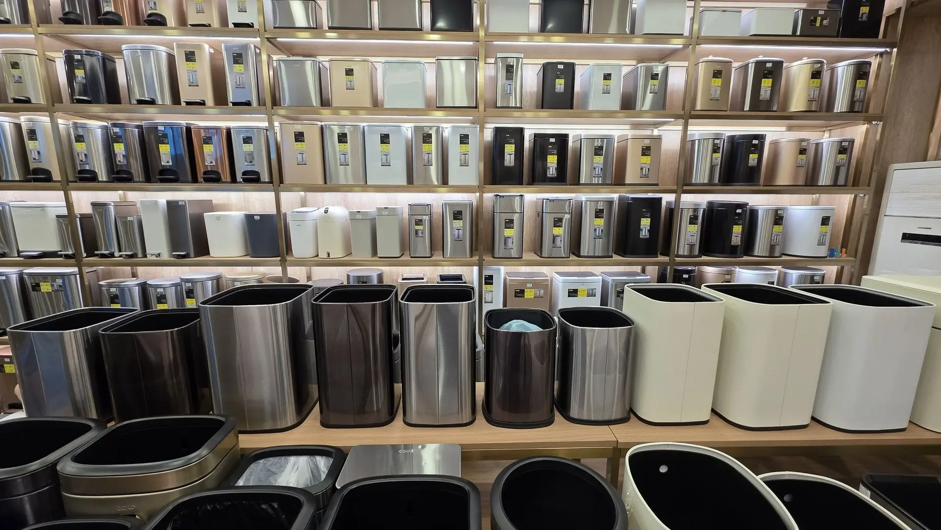 A wide variety of modern stainless steel and matte-colored kitchen trash cans displayed on showroom shelves.