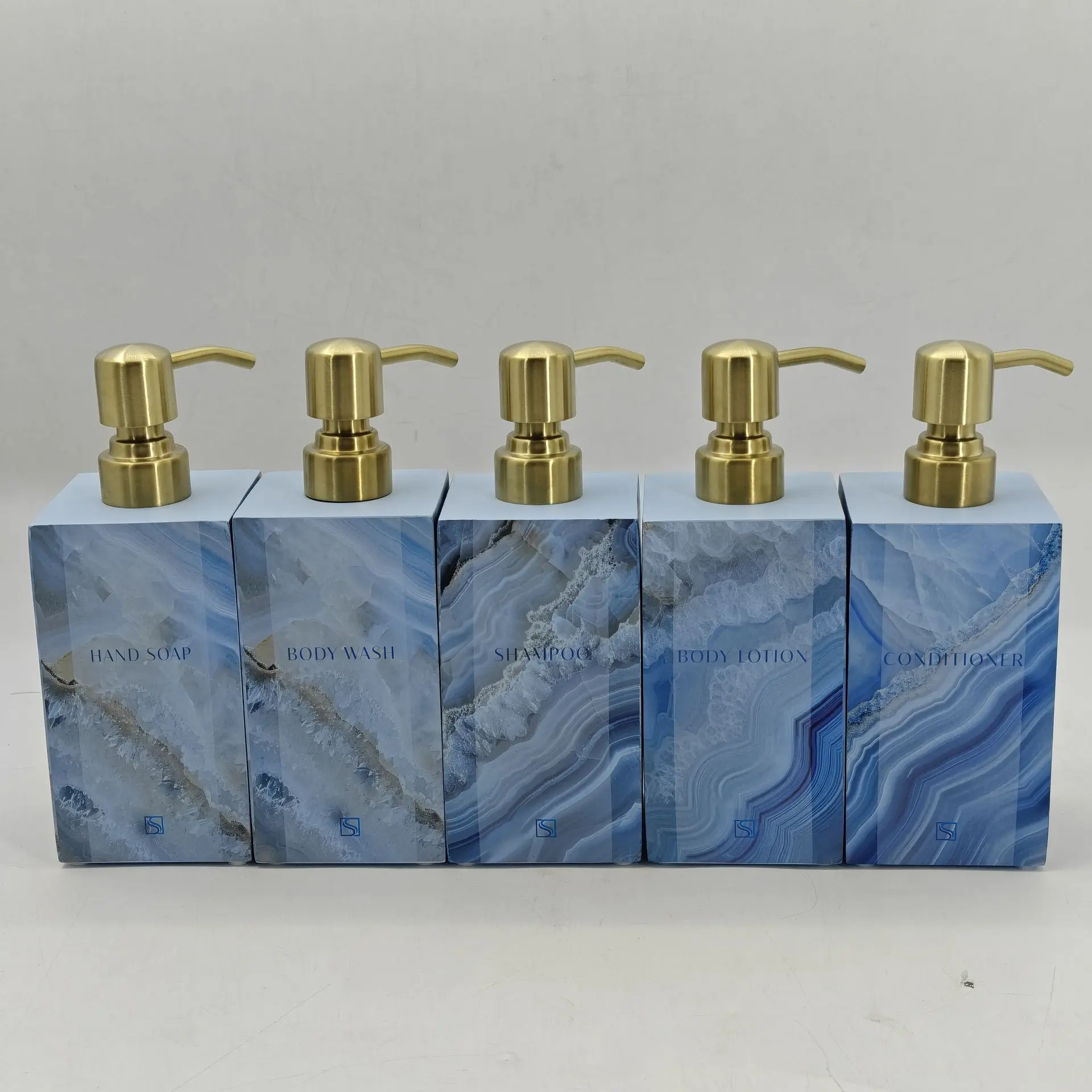 Five rectangular liquid soap dispensers made of blue marble-patterned resin featuring elegant gold-finished pump heads.