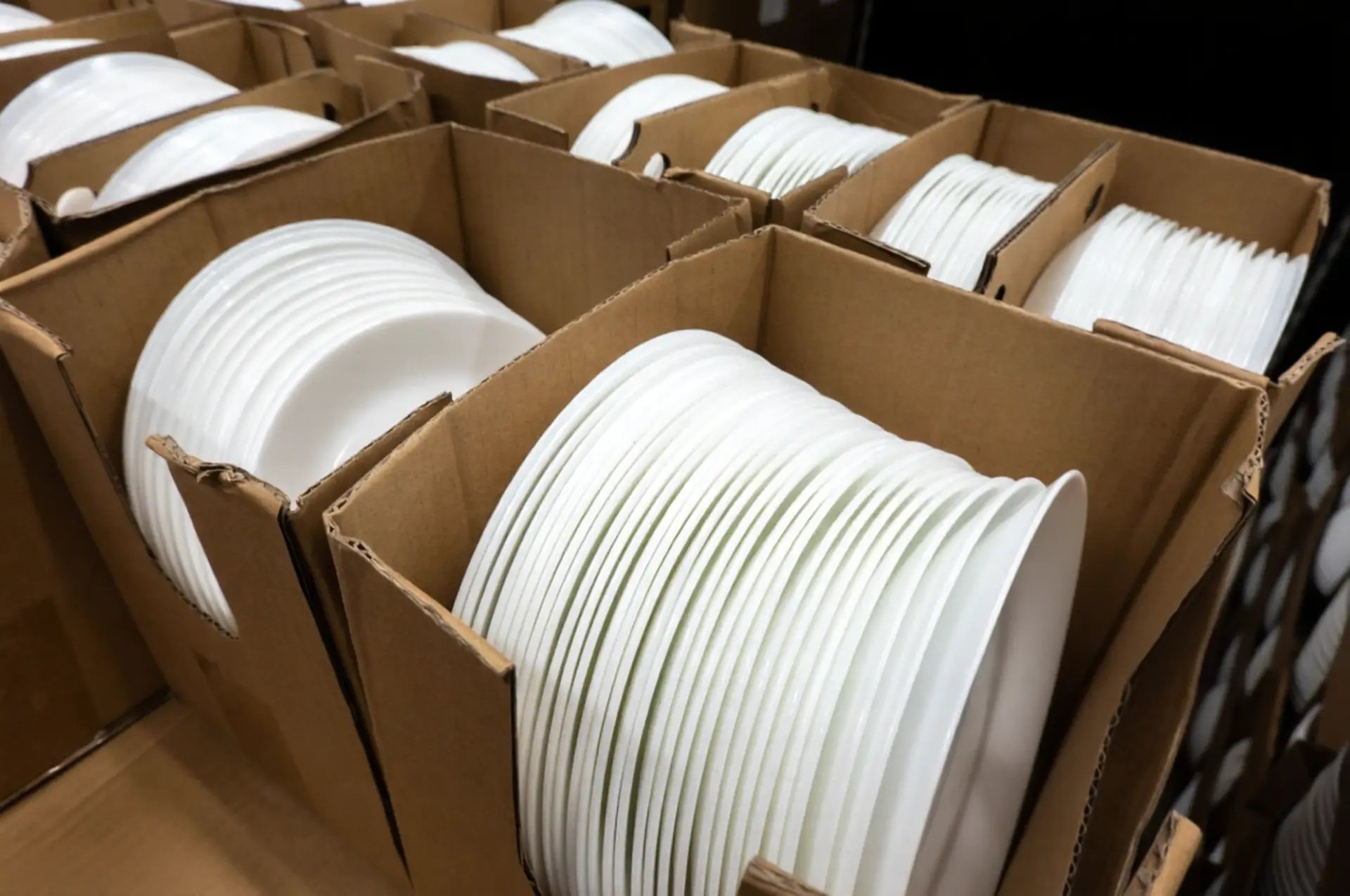 Warehouse inventory management for holiday peak season – Bulk dinnerware shipping. Stacked white ceramic dinner plates in cardboard boxes prepared for high-volume shipping during the holiday peak season.