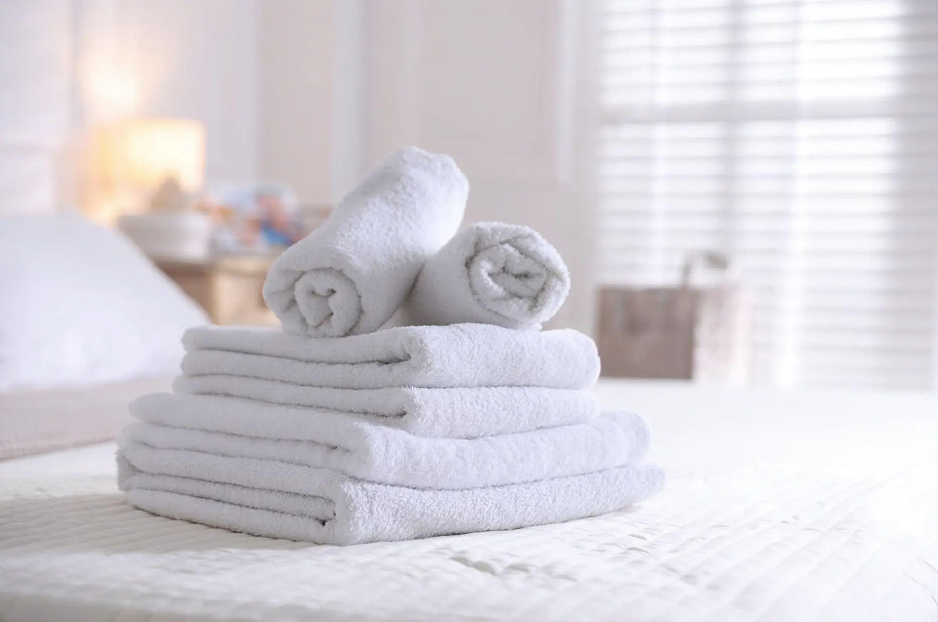 Stack of neatly folded white towels and linens on a hotel bed, representing high-quality OS&E hospitality supplies.