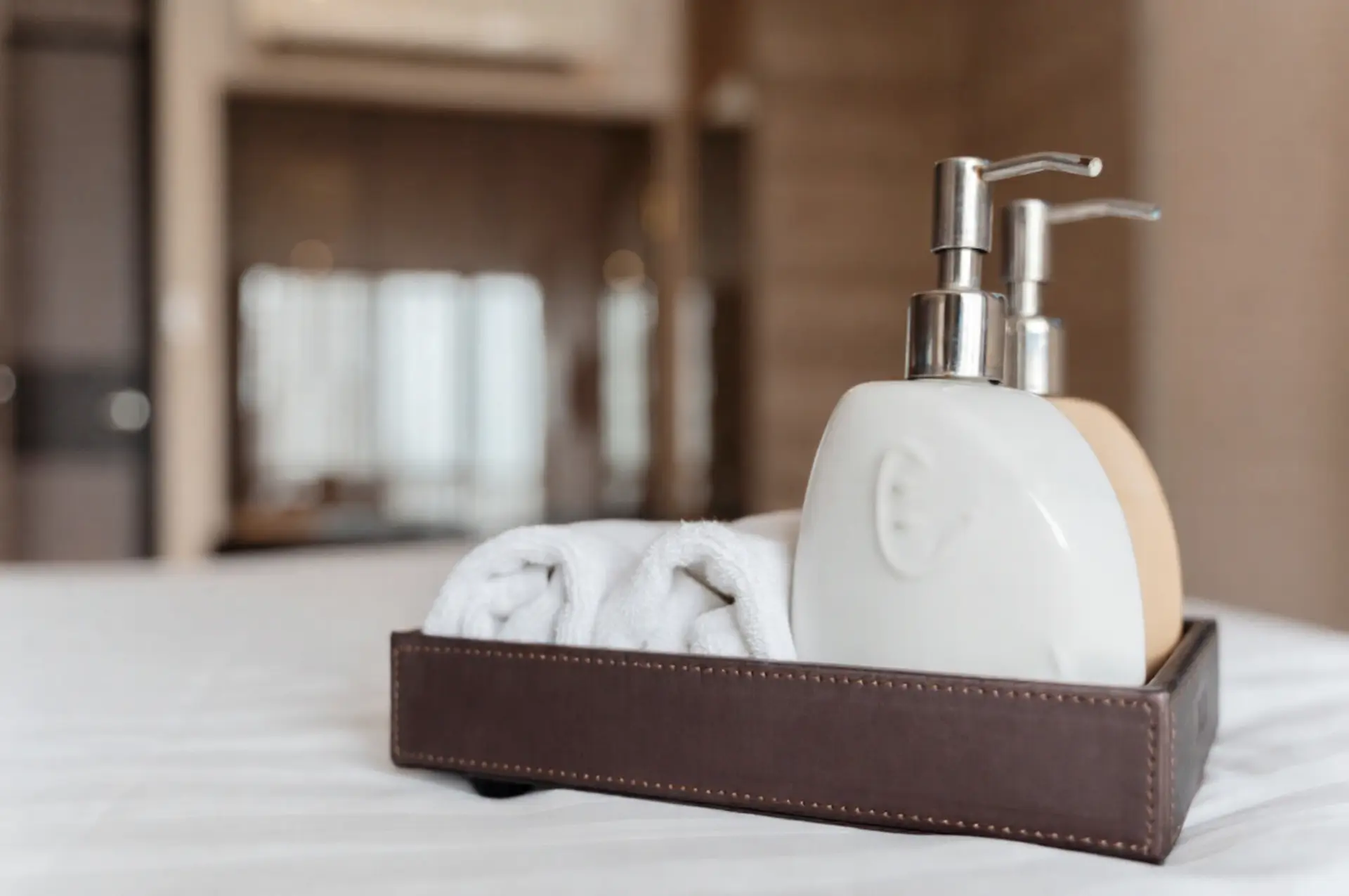 Modern white ceramic soap dispensers and rolled hand towels in a brown leather tray in China.