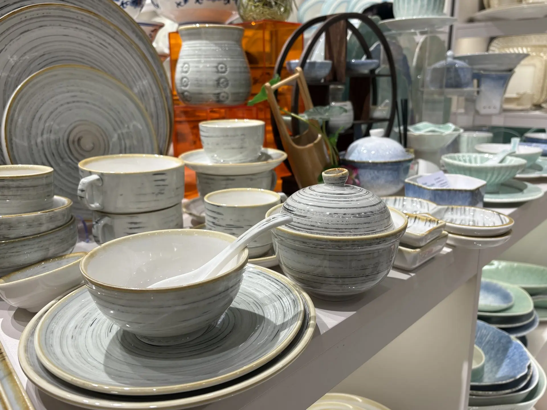 A display of grey and white hand-painted china dinnerware featuring swirl patterns, including bowls, plates, and a lidded tureen with a ceramic spoon.