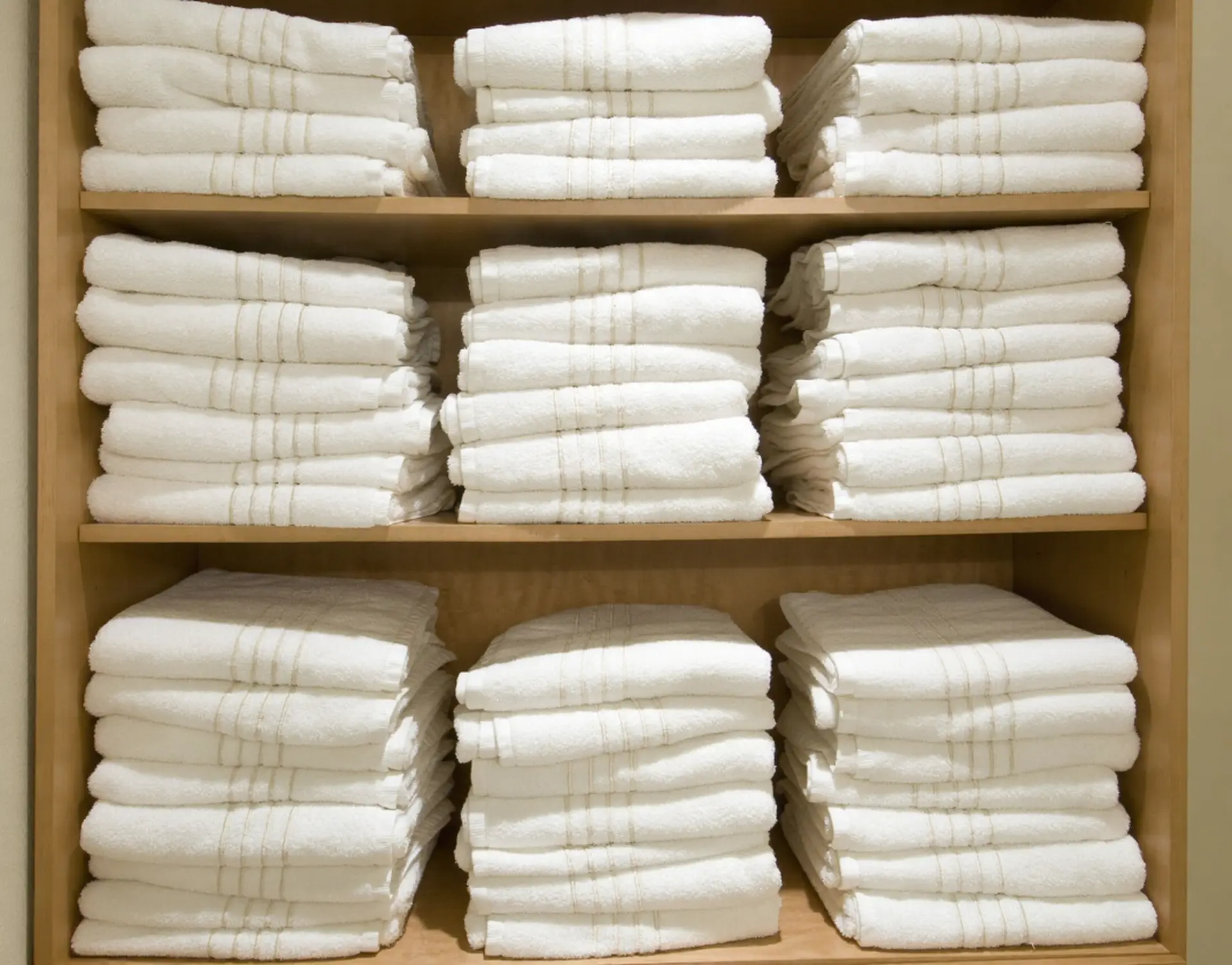 Neatly stacked white hotel towels on wooden shelves by World's OS&E in China.
