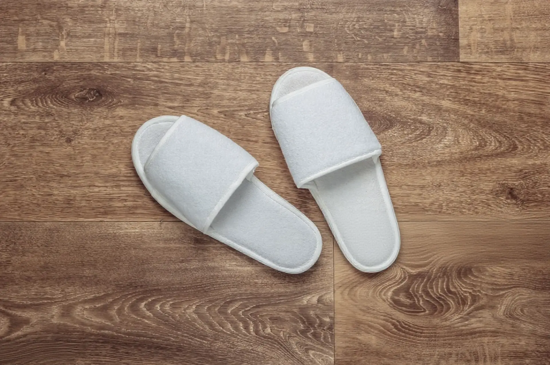 Comfortable white slippers – China OS&E hotel amenity White hotel slippers on wooden floor, China OS&E quality hospitality item