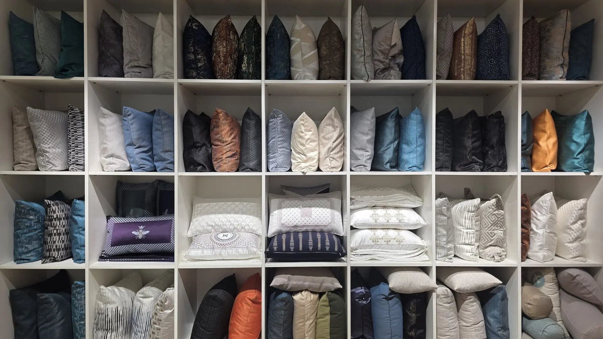 Showroom display of wholesale decorative pillows and soft furnishings in China A large white shelving unit in China filled with a variety of colorful decorative throw pillows and cushions in different fabrics and patterns