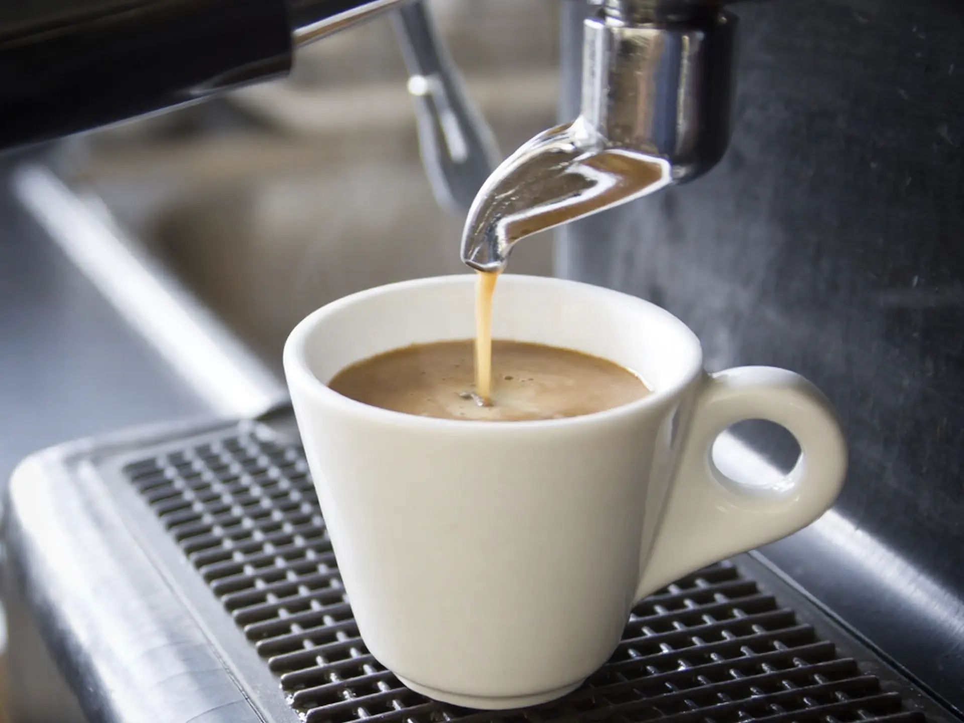 Close-up of fresh espresso being brewed into a white ceramic cup from a commercial espresso machine manufactured in China.