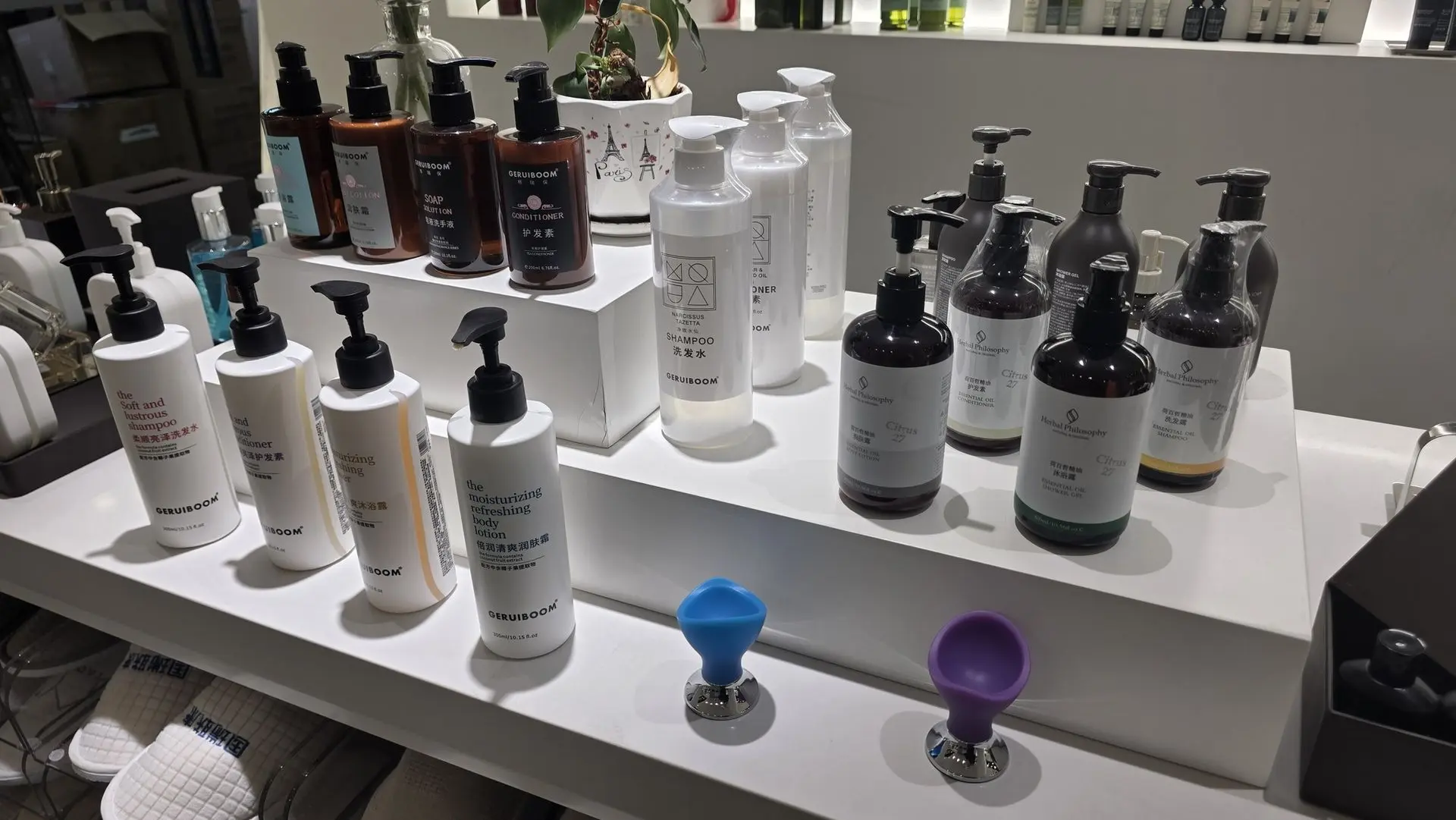 A variety of luxury hotel toiletries and bath products including shampoos, conditioners, and body lotions displayed on a white tiered shelf.