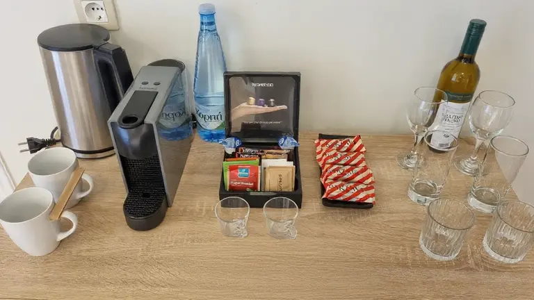 Professional hotel guest room beverage station featuring coffee machine, kettle, and China OS&E glassware and mugs on a wooden table.