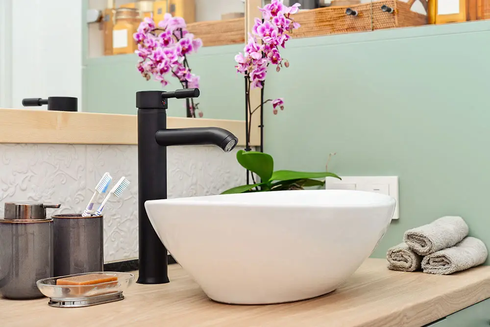 Modern matte black faucet and white vessel sink in a guestroom bathroom from China with orchid decor.