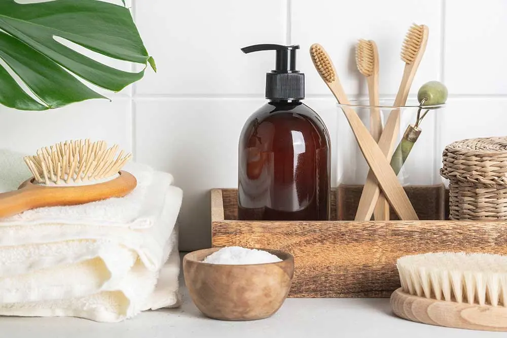 Sustainable guestroom bathroom accessories including bamboo toothbrushes, a wooden hairbrush, and natural soap dispenser sourced from China.
