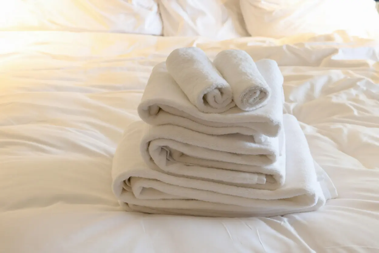 Professionally folded white cotton towels stacked on a white duvet, showcasing luxury China OS&E bedding supplies for hotel brand standard compliance.