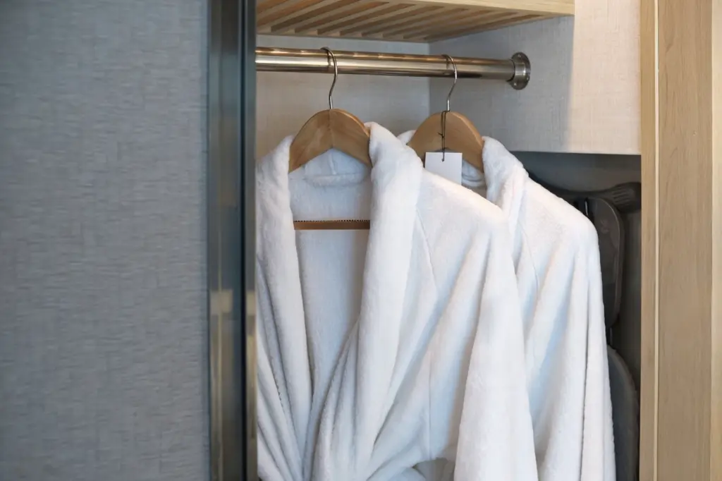 Two plush white hotel bathrobes hanging on wooden hangers in a closet, representing luxury China OS&E guest room amenities.