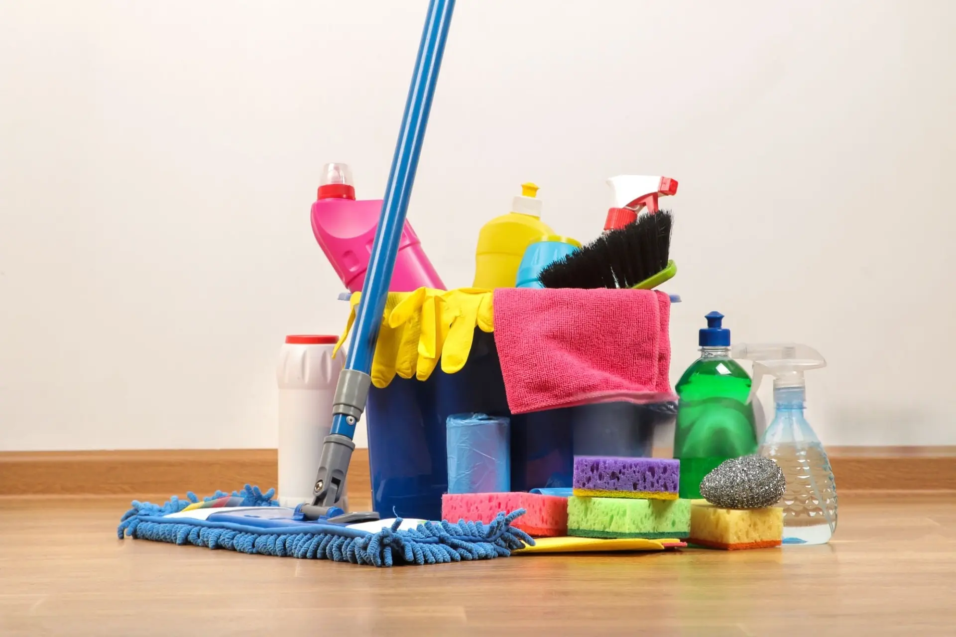 A comprehensive set of China OS&E cleaning supplies including a blue microfiber mop, colorful detergent bottles, sponges, and rubber gloves in a bucket on a wooden floor.