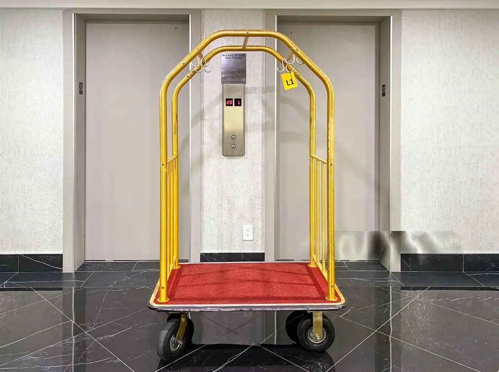 Premium Gold Hotel Bellman Cart - High-Quality OS&E China Supplies Gold birdcage bellman luggage cart with red carpeted base, a professional OS&E China hospitality equipment essential, positioned in front of hotel elevators.