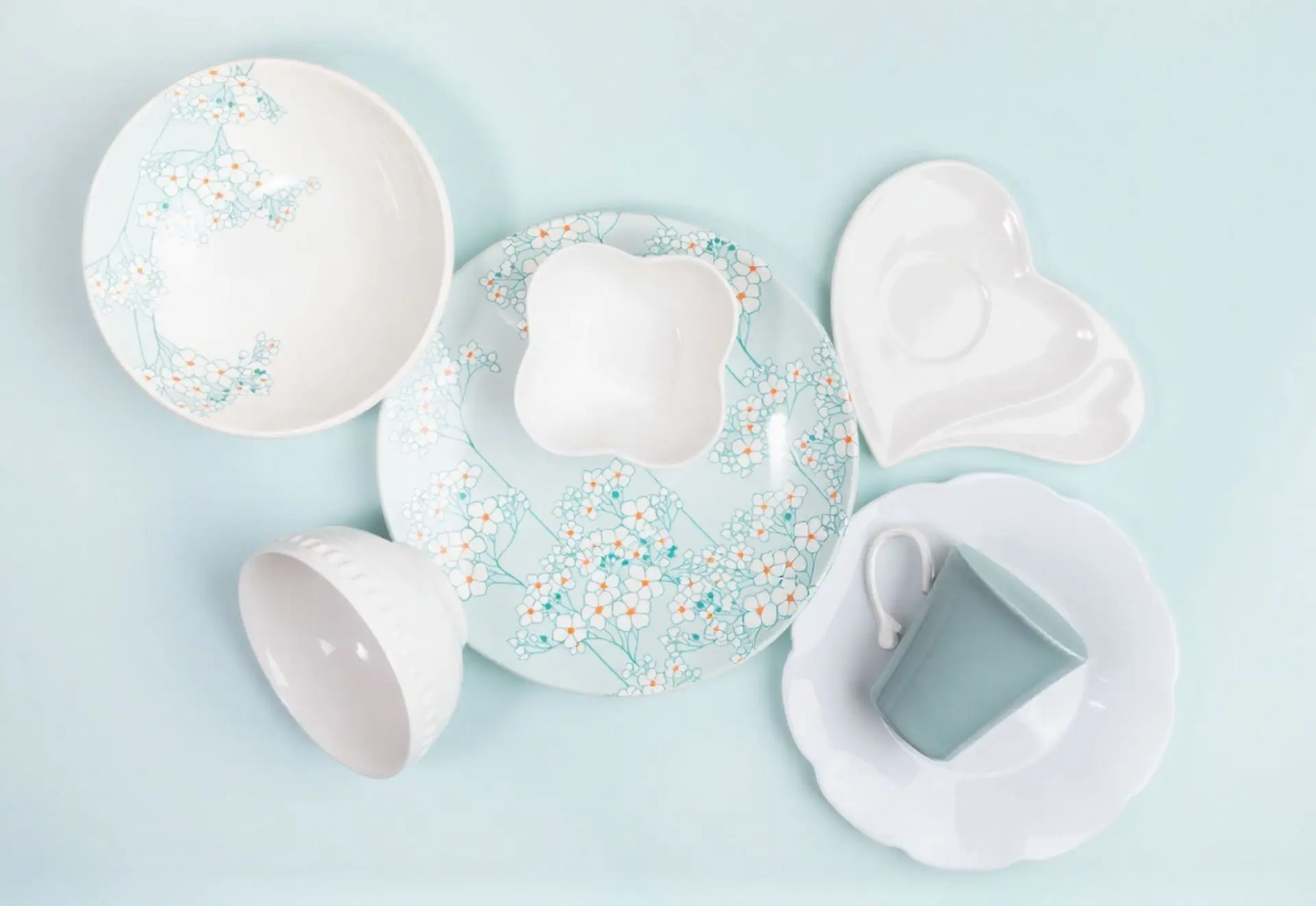 Decorative melamine tableware from China featuring a light blue floral pattern on plates and bowls, accompanied by a heart-shaped saucer and a sage green mug.