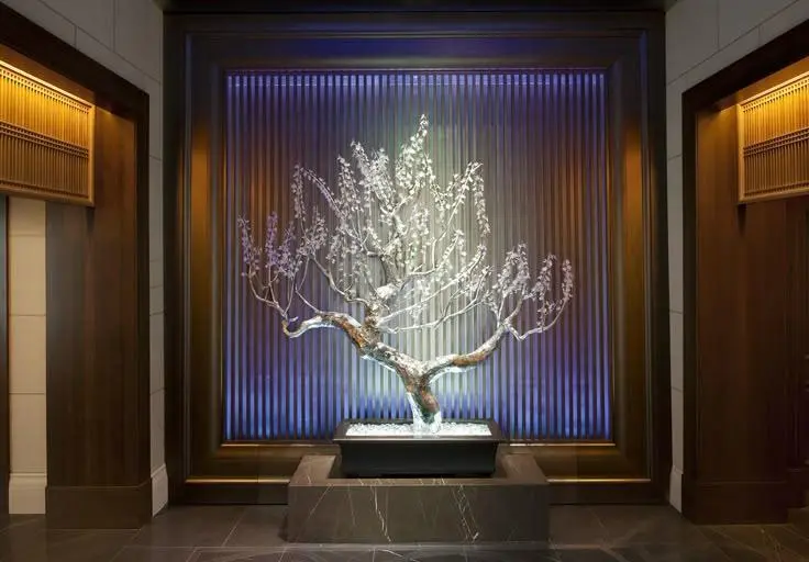 A glowing crystalline bonsai tree sculpture illuminated against a ribbed blue backdrop, highlighting Custom Sculptures from China in a modern luxury interior.