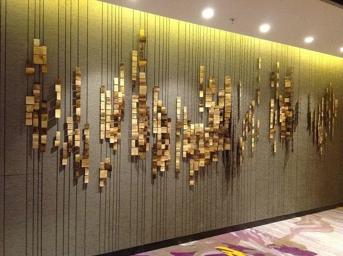 A contemporary wall-mounted installation consisting of small gold metal squares suspended on thin vertical wires, representing Custom Sculptures from China in a modern hallway