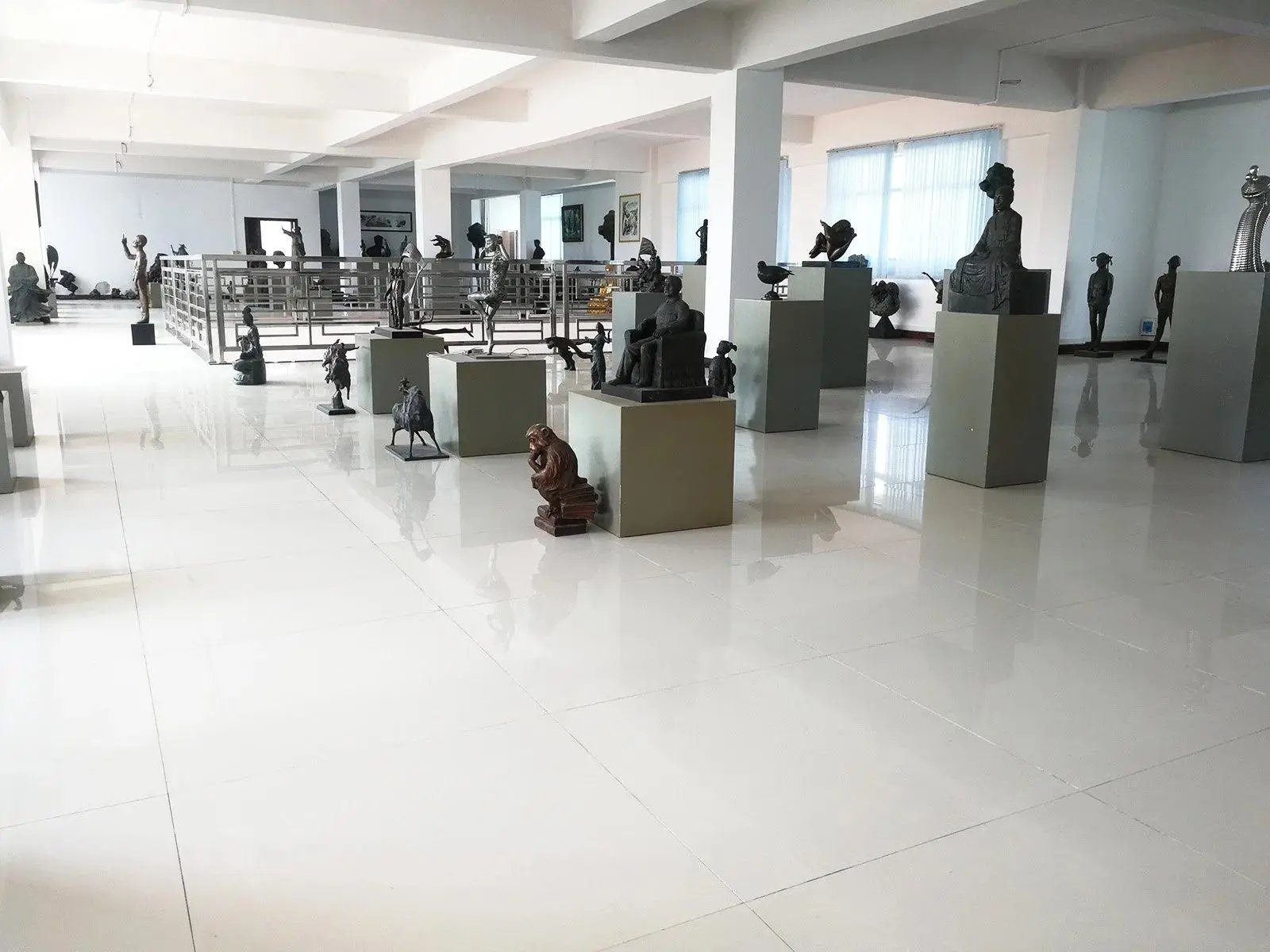 A spacious art gallery showroom featuring a diverse collection of bronze and metal Custom Sculptures from China displayed on grey pedestals.