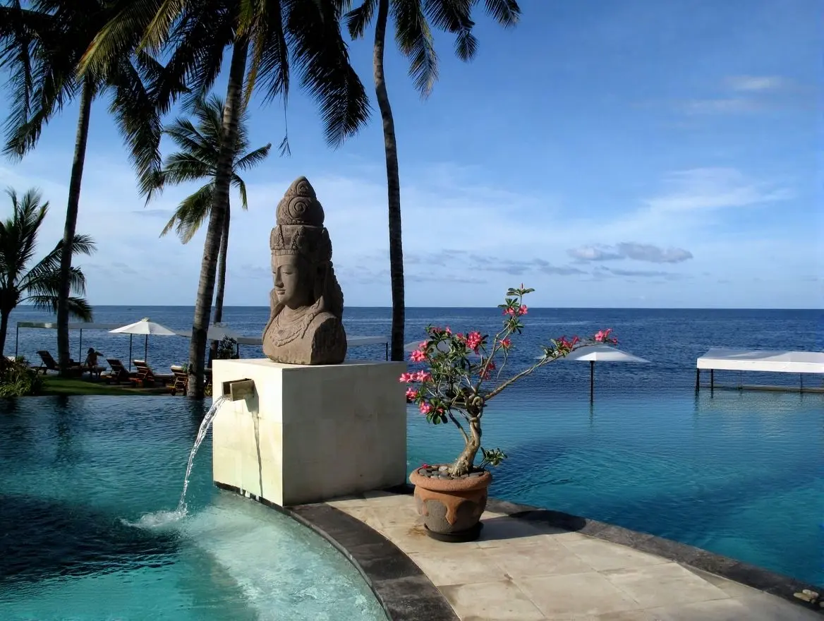 A serene infinity pool overlooking the ocean, featuring a stone Buddha bust water fountain and tropical palm trees, demonstrating Custom Sculptures from China for luxury resorts.