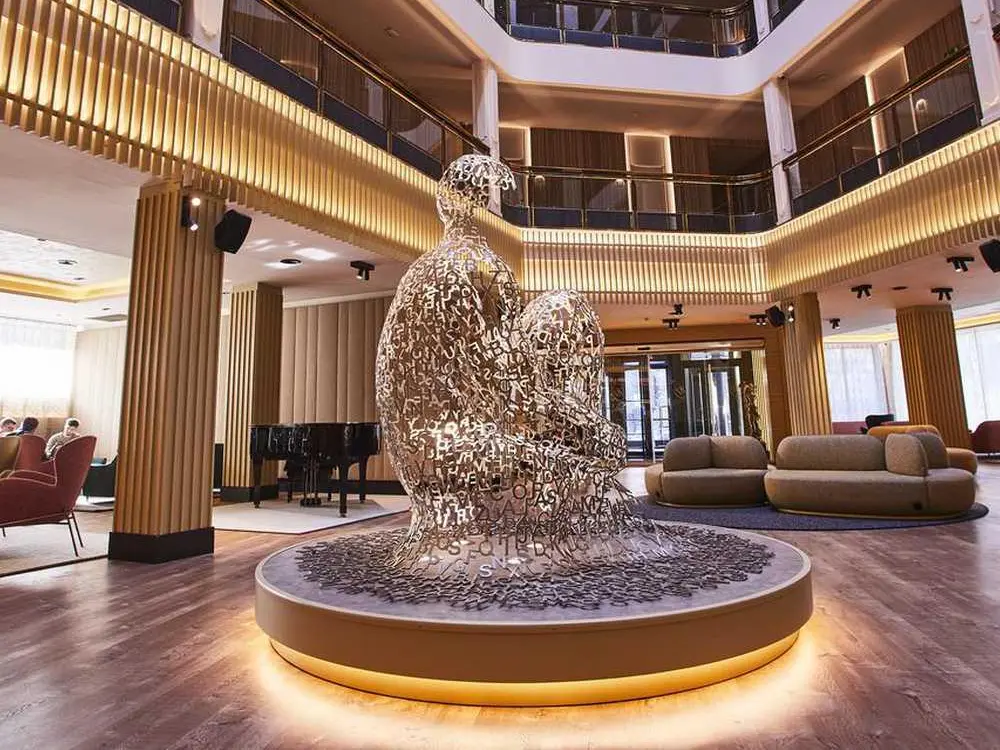 A large-scale stainless steel figure made of intricate metal letters, showcasing Custom Sculptures from China in a multi-level luxury hotel atrium.