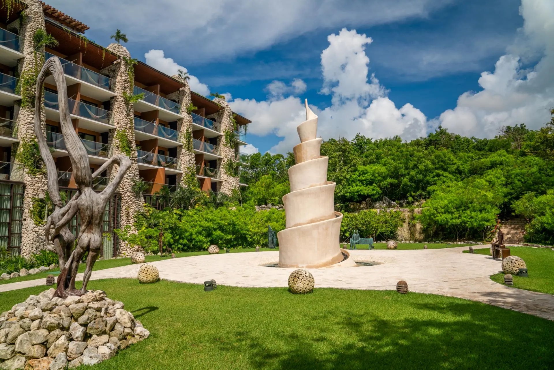An outdoor resort garden featuring a large white spiral monument and organic wood figures, showcasing Custom Sculptures from China in a tropical landscape.
