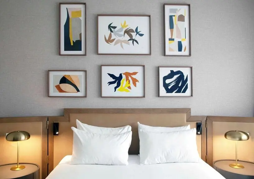 Modern Bedroom Decor with Abstract Art Gallery Wall and Brass Lamps Modern bedroom decor featuring a symmetrical gallery wall with abstract botanical and geometric prints above a padded headboard, flanked by round bedside tables with brass mushroom lamps
