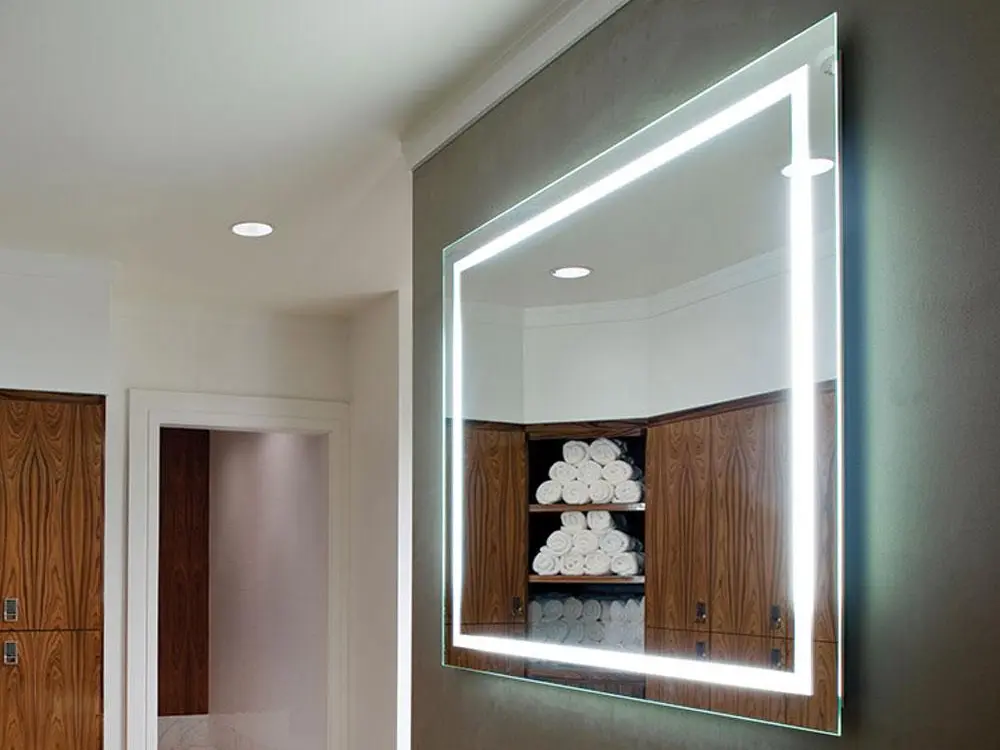 Backlit LED Mirror Decor for Guest Rooms and Bathrooms Modern rectangular wall mirror with integrated LED backlighting reflecting wooden shelves stocked with rolled white towels in a guest room or bathroom setting