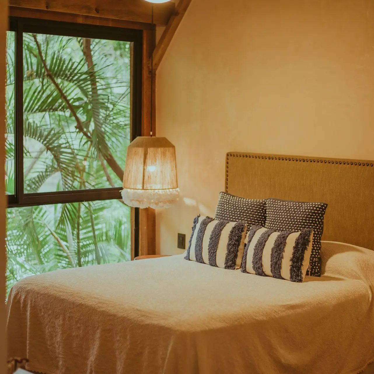 Cozy Upholstered Chinese Headboard with Tropical View Simple upholstered Chinese headboard with nailhead trim in a cozy bedroom overlooking tropical palm trees