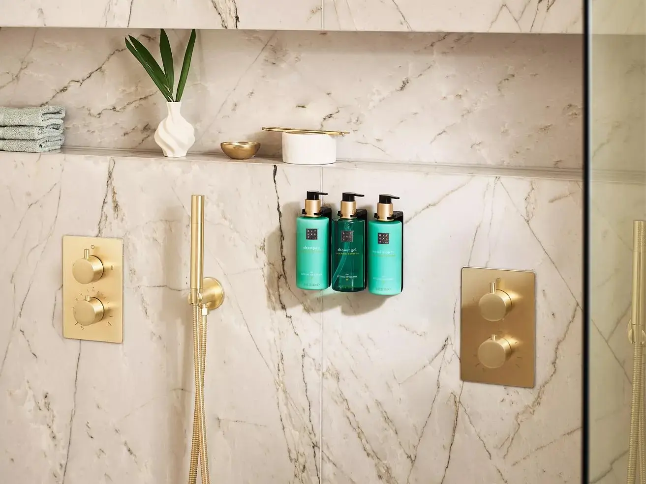 Luxury Hotel Room Toiletries Wall Dispenser Set Wall-mounted hotel room toiletries and pump dispensers with gold shower fixtures against a marble bathroom wall