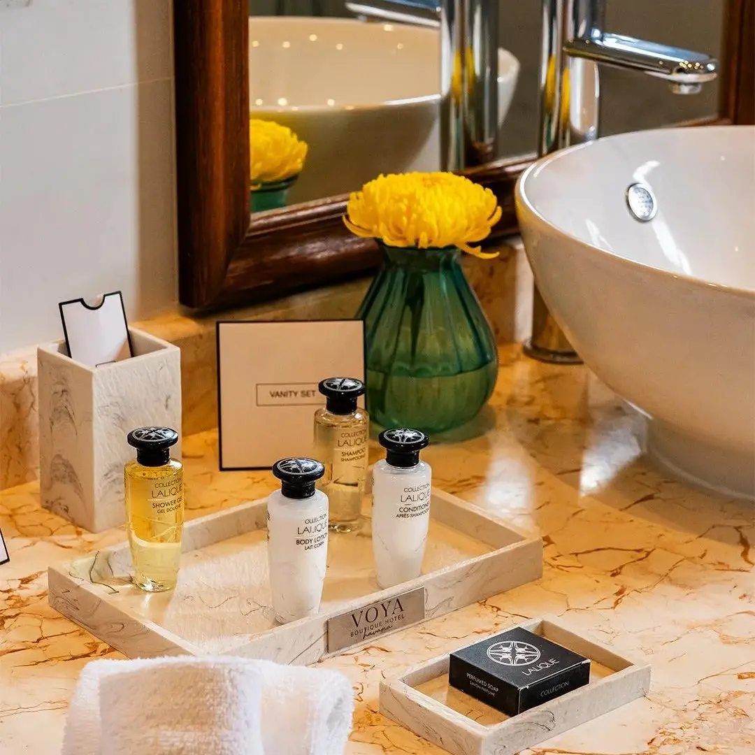 Luxury VOYA Hotel Room Toiletries Tray Setup VOYA hotel room toiletries bottles, vanity set box, and guest soap arranged on a marble vanity tray with a bathroom sink in the background