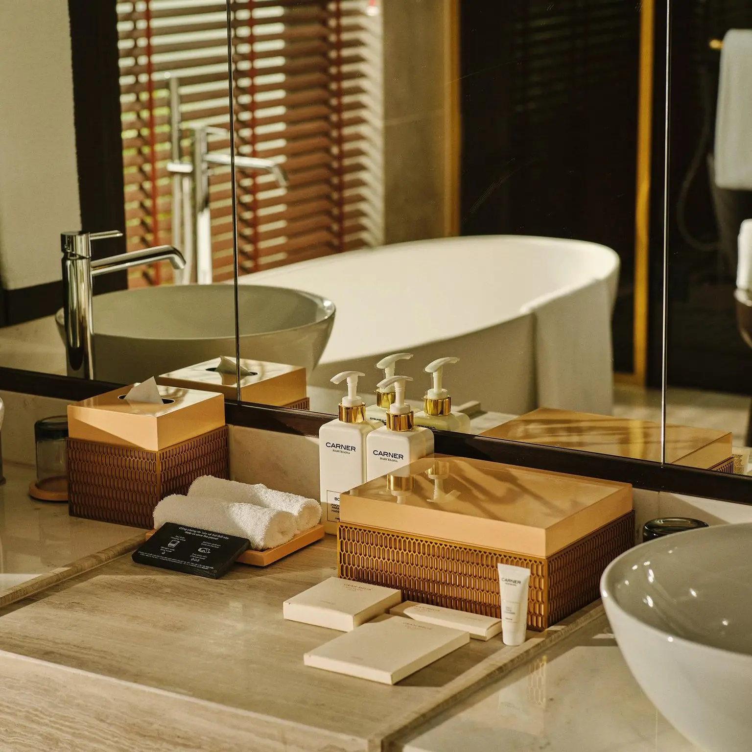 Luxury Hotel Room Toiletries & Amenity Tray Setup Elegant hotel room toiletries set including pump dispensers, amenity boxes, and vanity trays displayed on a marble bathroom vanity with a bathtub in the background